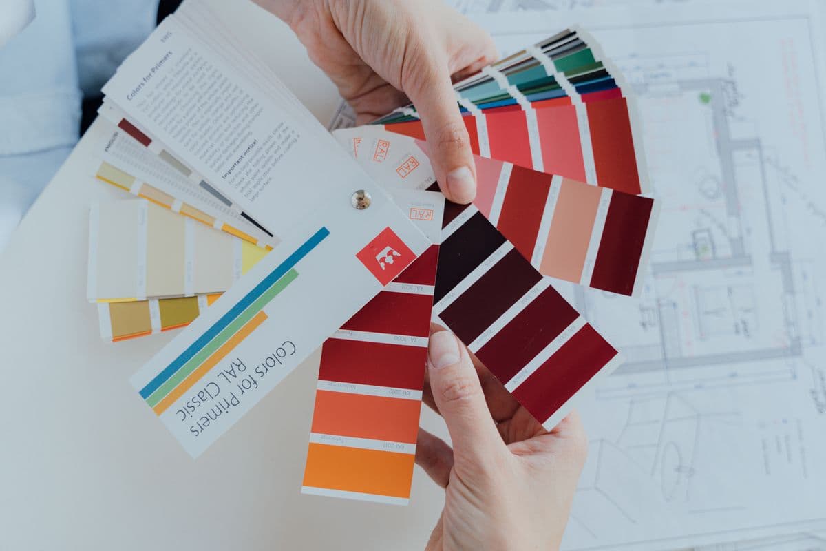 Hands holding fan decks of paint color swatches over a floor plan