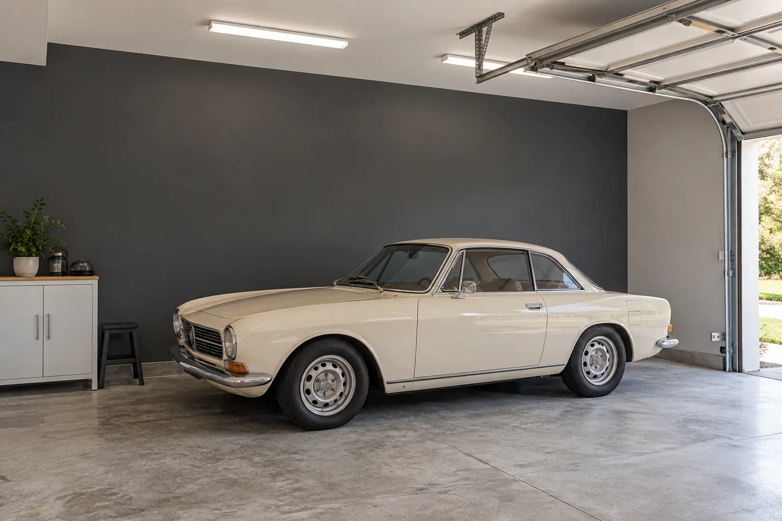 Charcoal gray garage accent wall behind a cream vintage coupe, with white cabinets and gray flooring