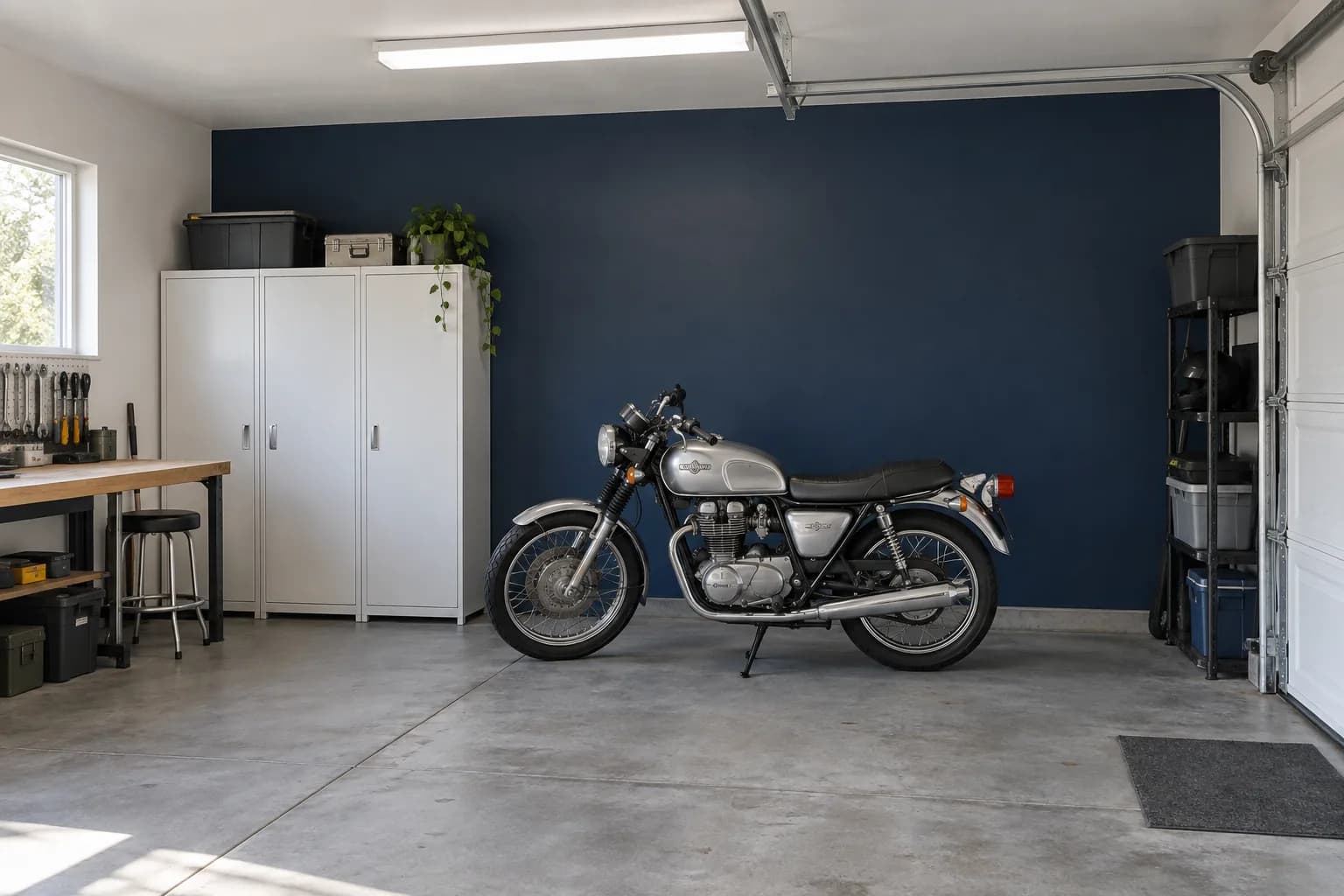 Navy garage accent wall behind a silver motorcycle, with white storage cabinets and gray concrete flooring
