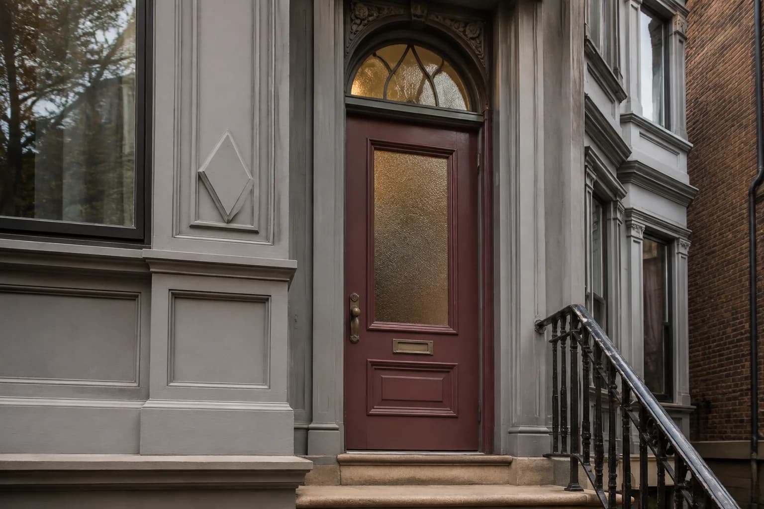 Tall burgundy Victorian door with textured glass and an arched transom beside ornate gray trim and an iron stair rail