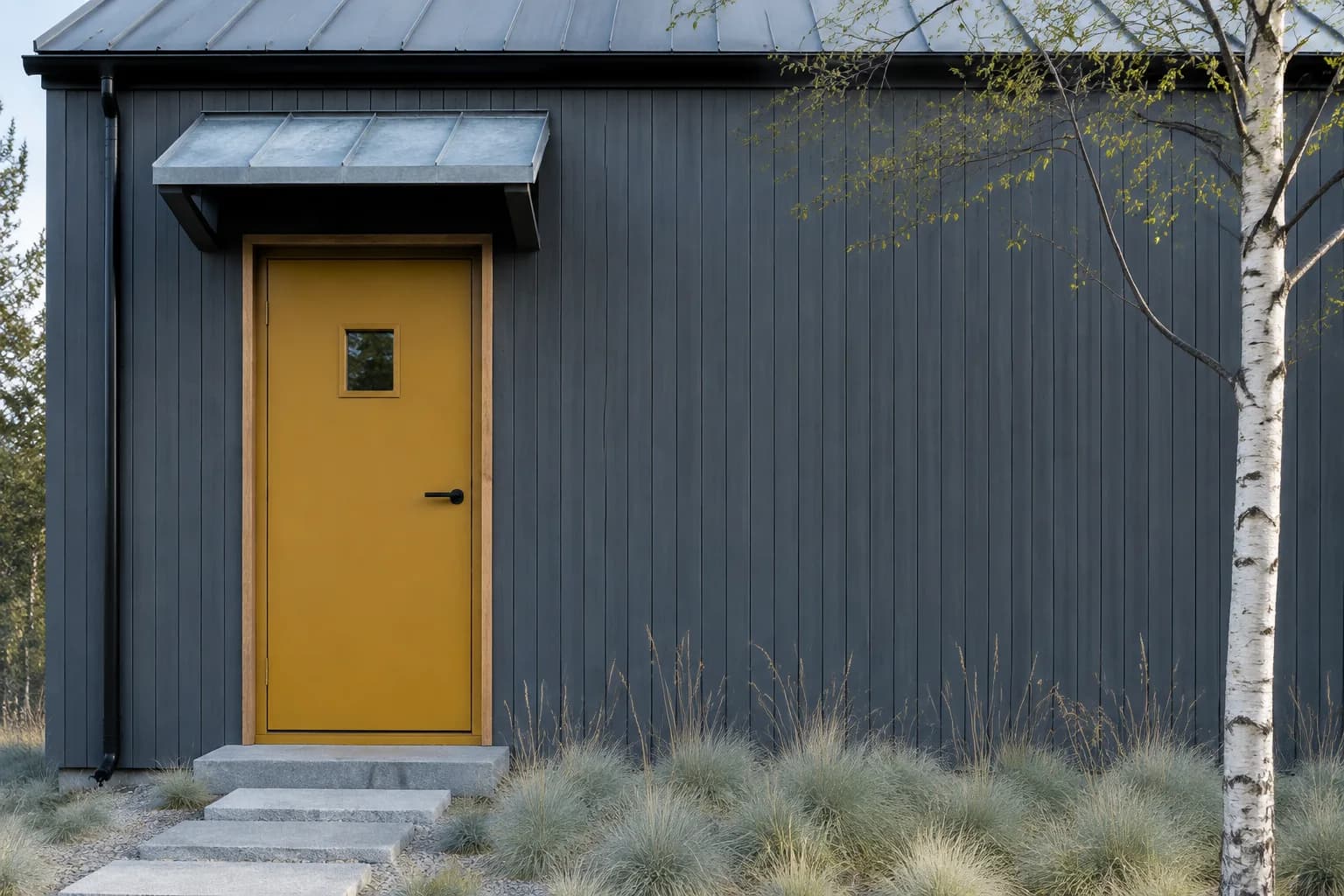 Mustard yellow door with a small square window on a dark gray Scandinavian-style timber house with a metal canopy