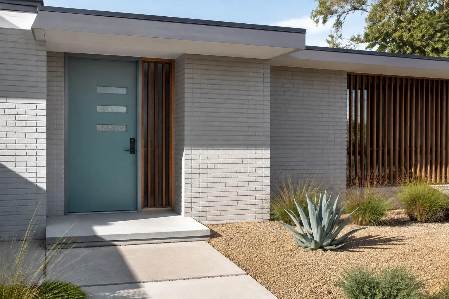 Teal mid-century door with three horizontal glass inserts on a gray painted-brick ranch with a timber screen