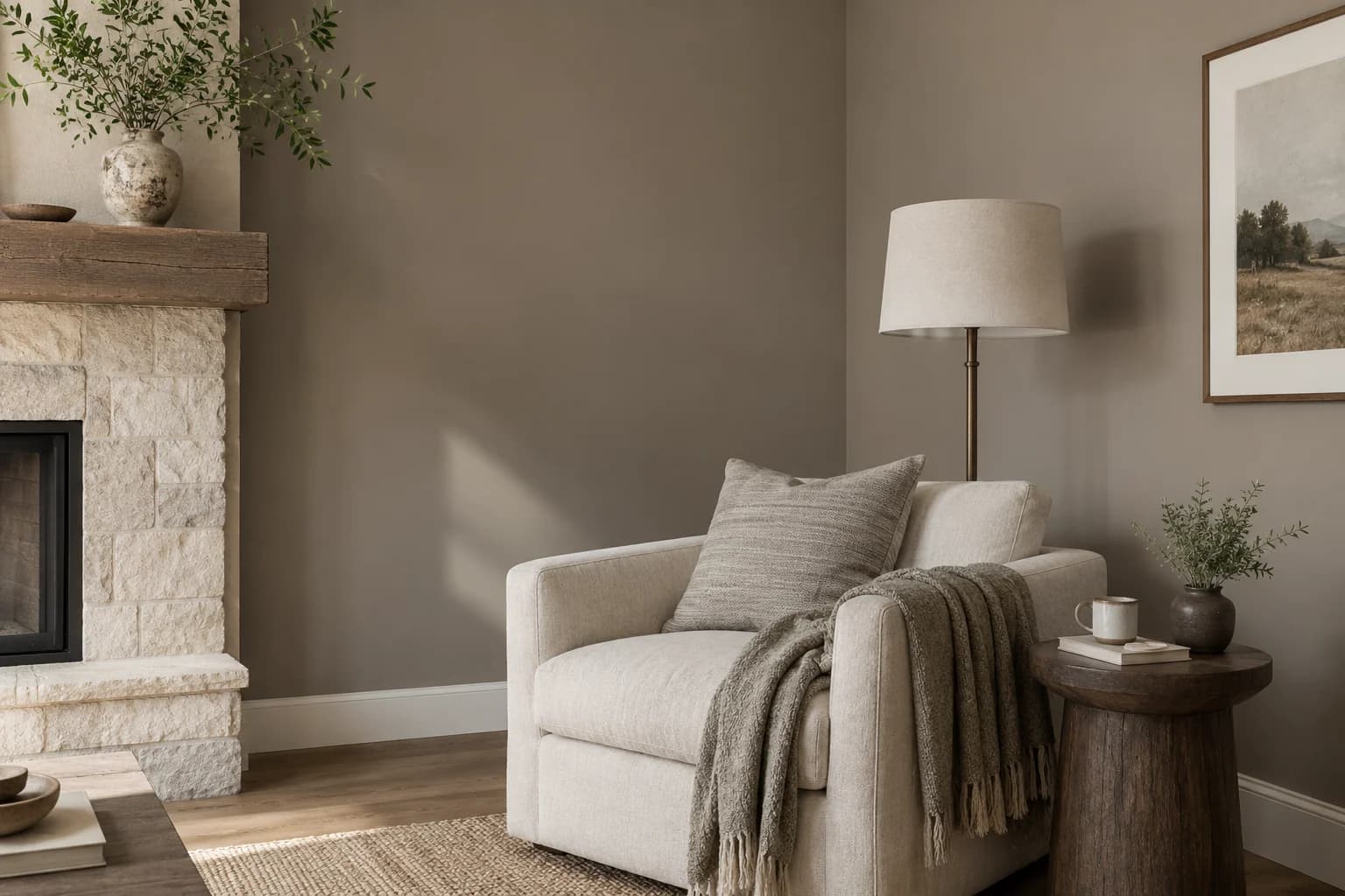 Coin salon aux murs taupe avec fauteuil crème et cheminée en pierre claire